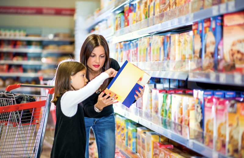 uma mãe avaliando um rótulo de embalagem para filha no supermercado
